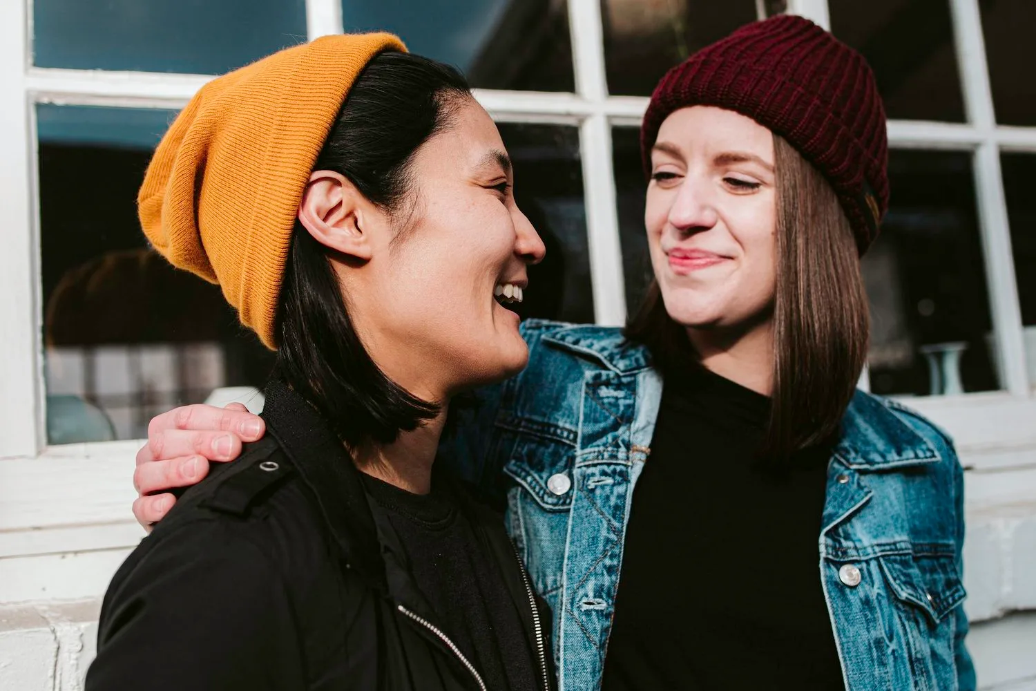 Two friends in knit hats smiling at each other outdoors