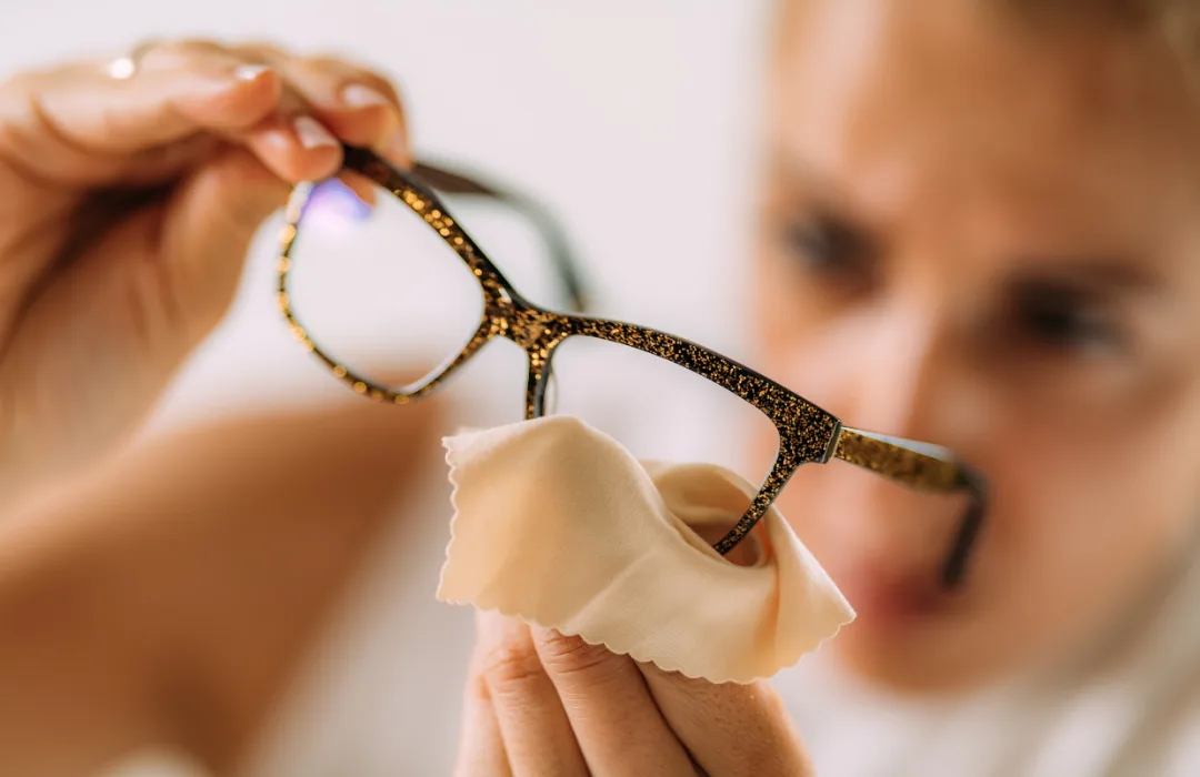 Close-up of a hand holding a pair of eyeglasses, face blurred behind