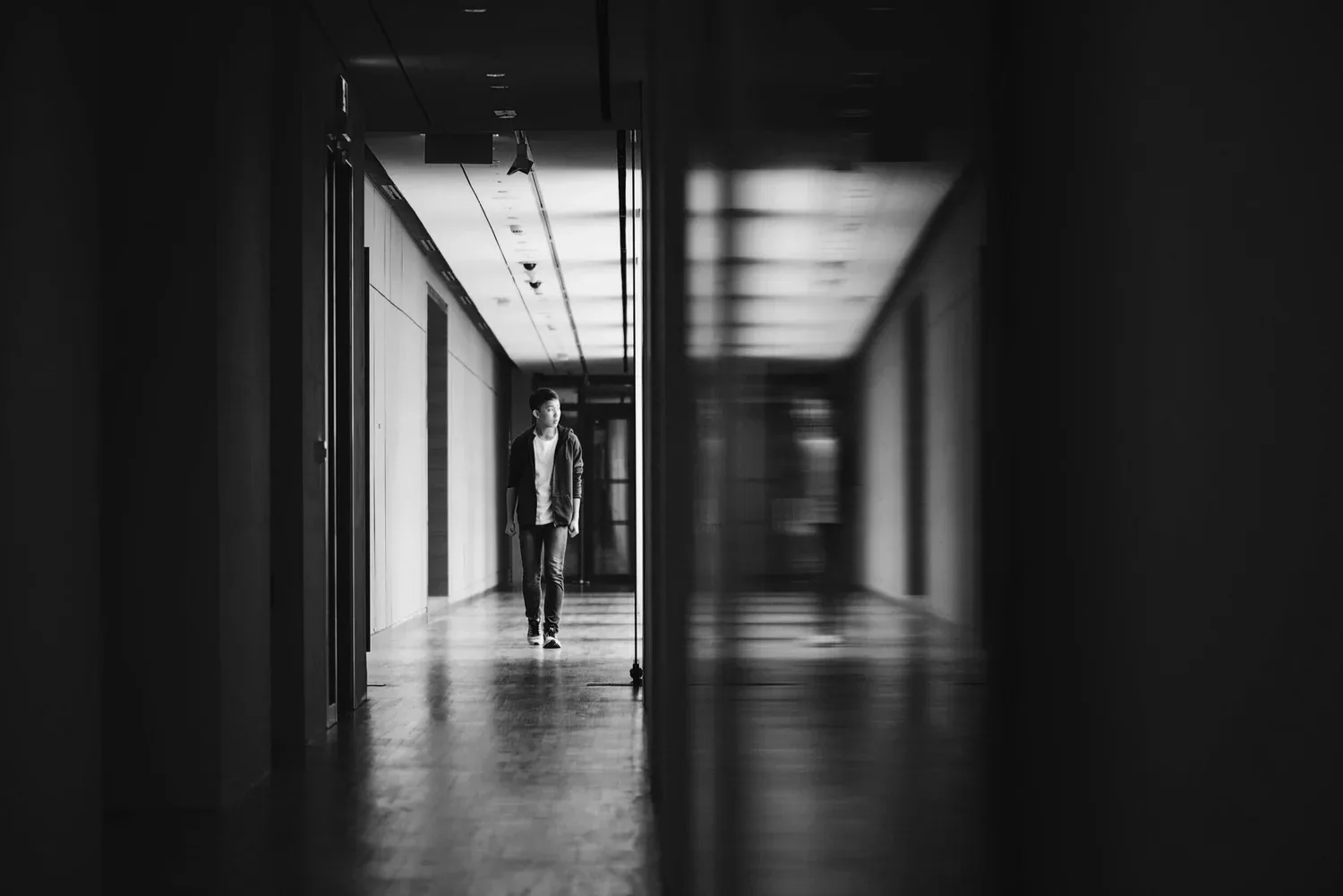 Black-and-white photo of a person standing at the end of a long, dark hallway