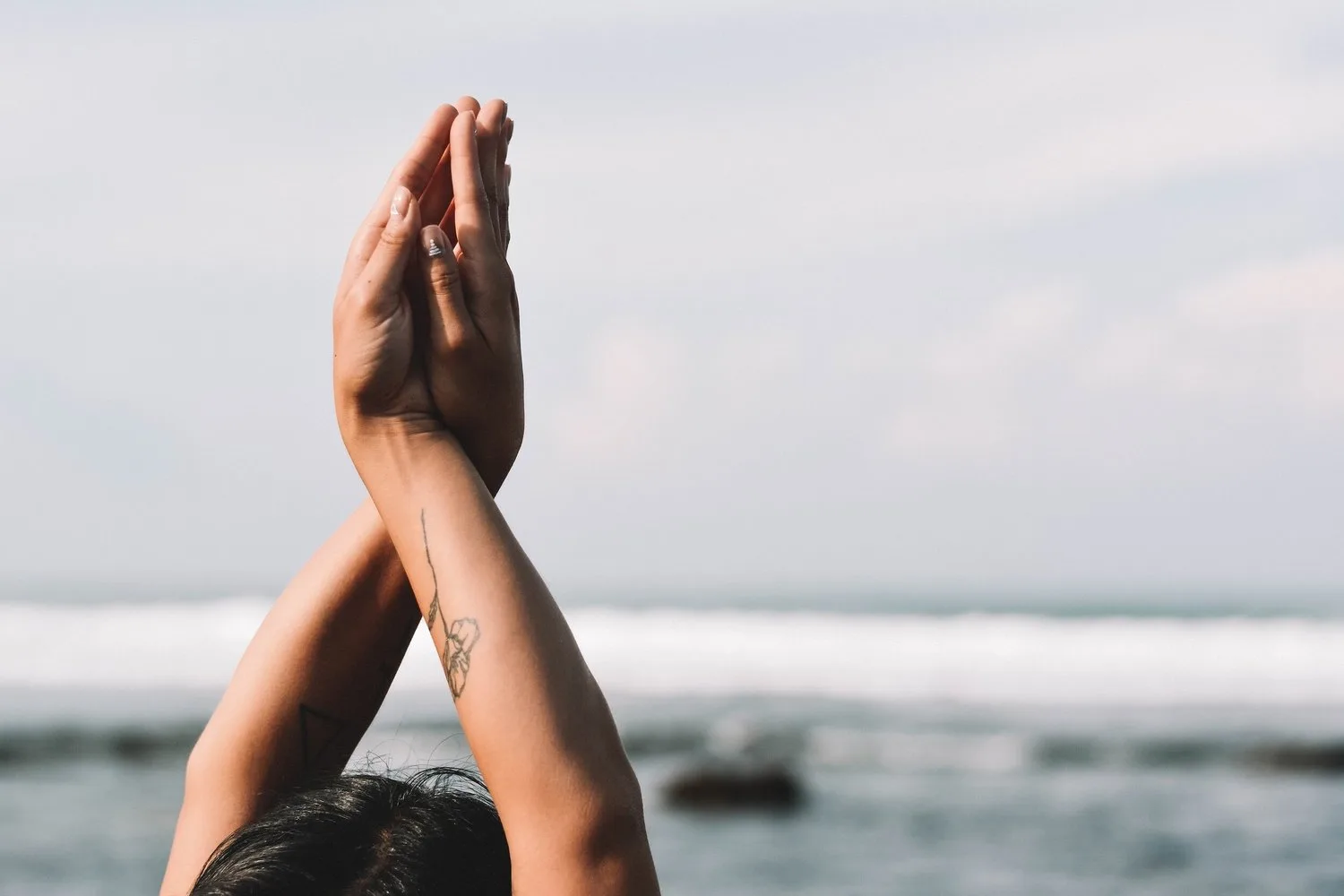 Hands pressed together overhead against a seaside backdrop
