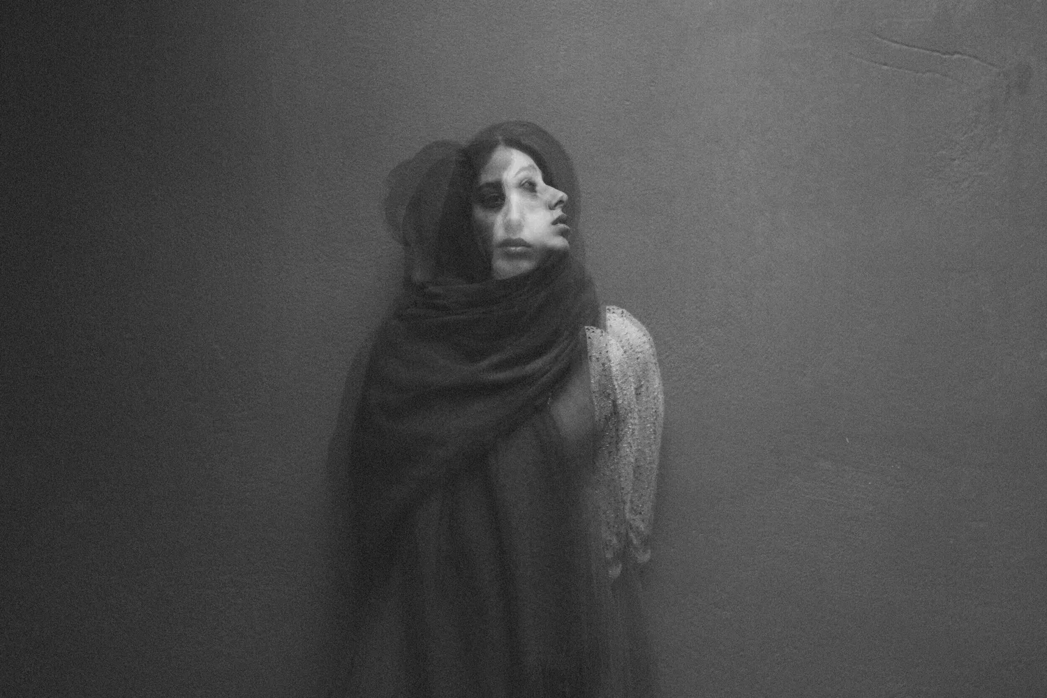 Black-and-white photo of a woman wrapped in a blanket against a dark wall