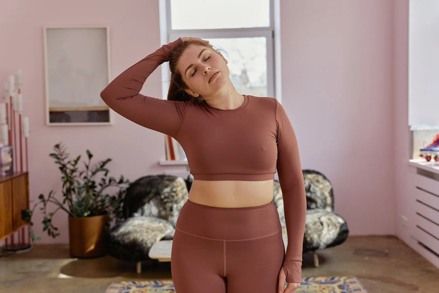 Woman in athletic wear stretching her neck with a hand on her head at home