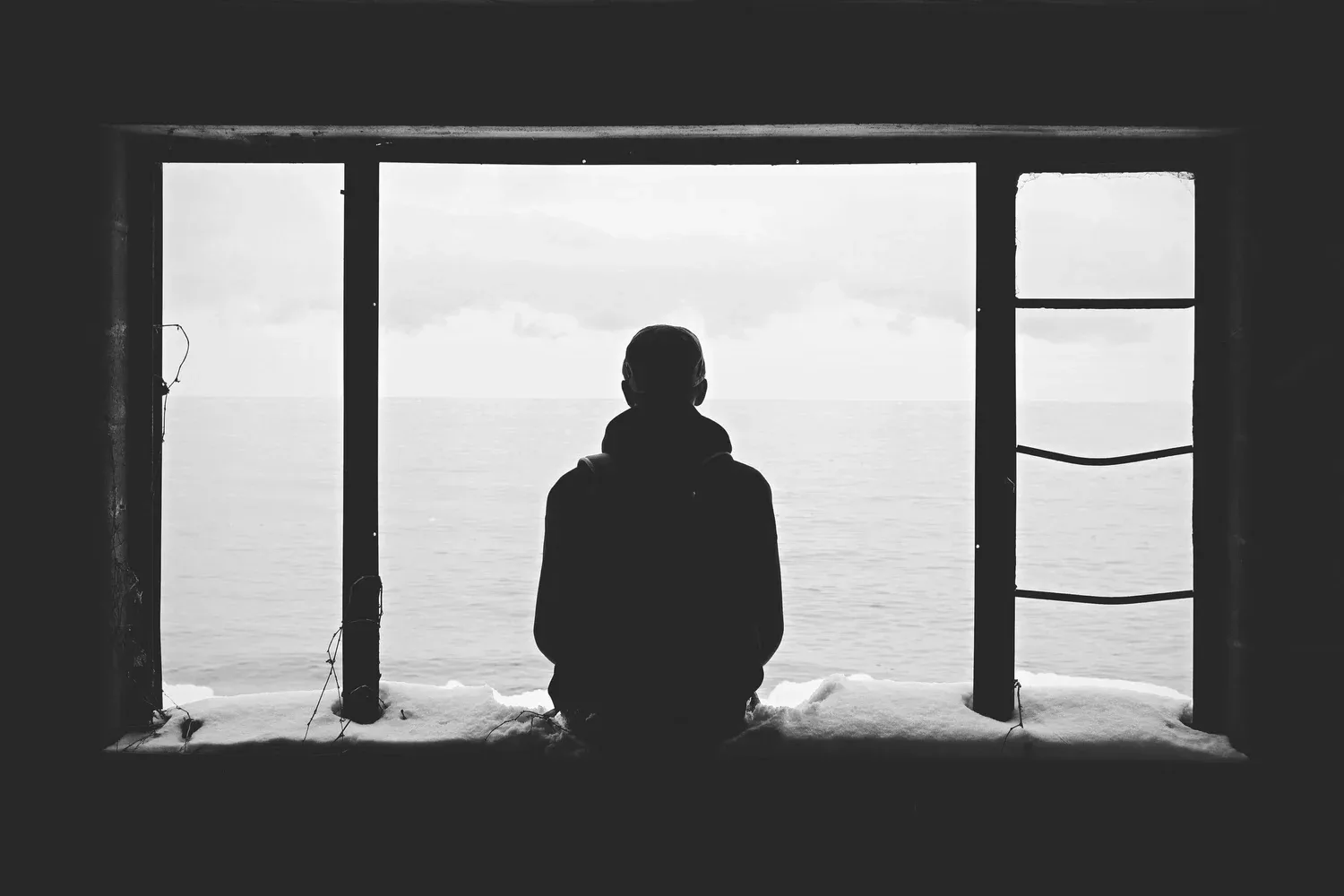 Silhouette of a person seated at a large window looking out at the water