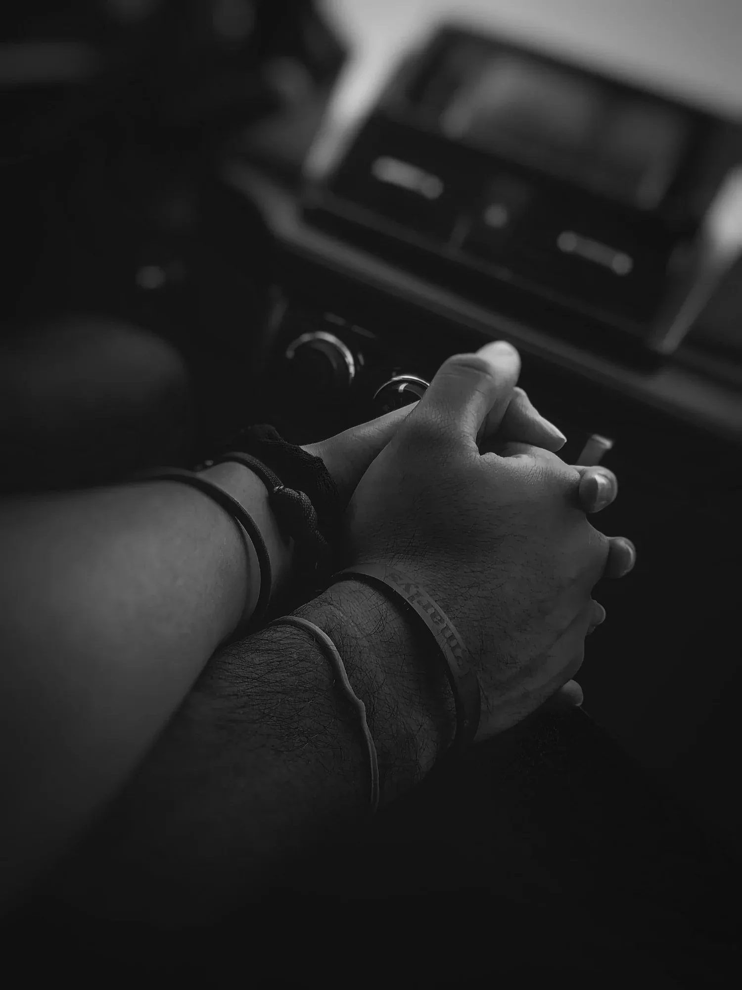 Black-and-white close-up of two people holding hands in a car
