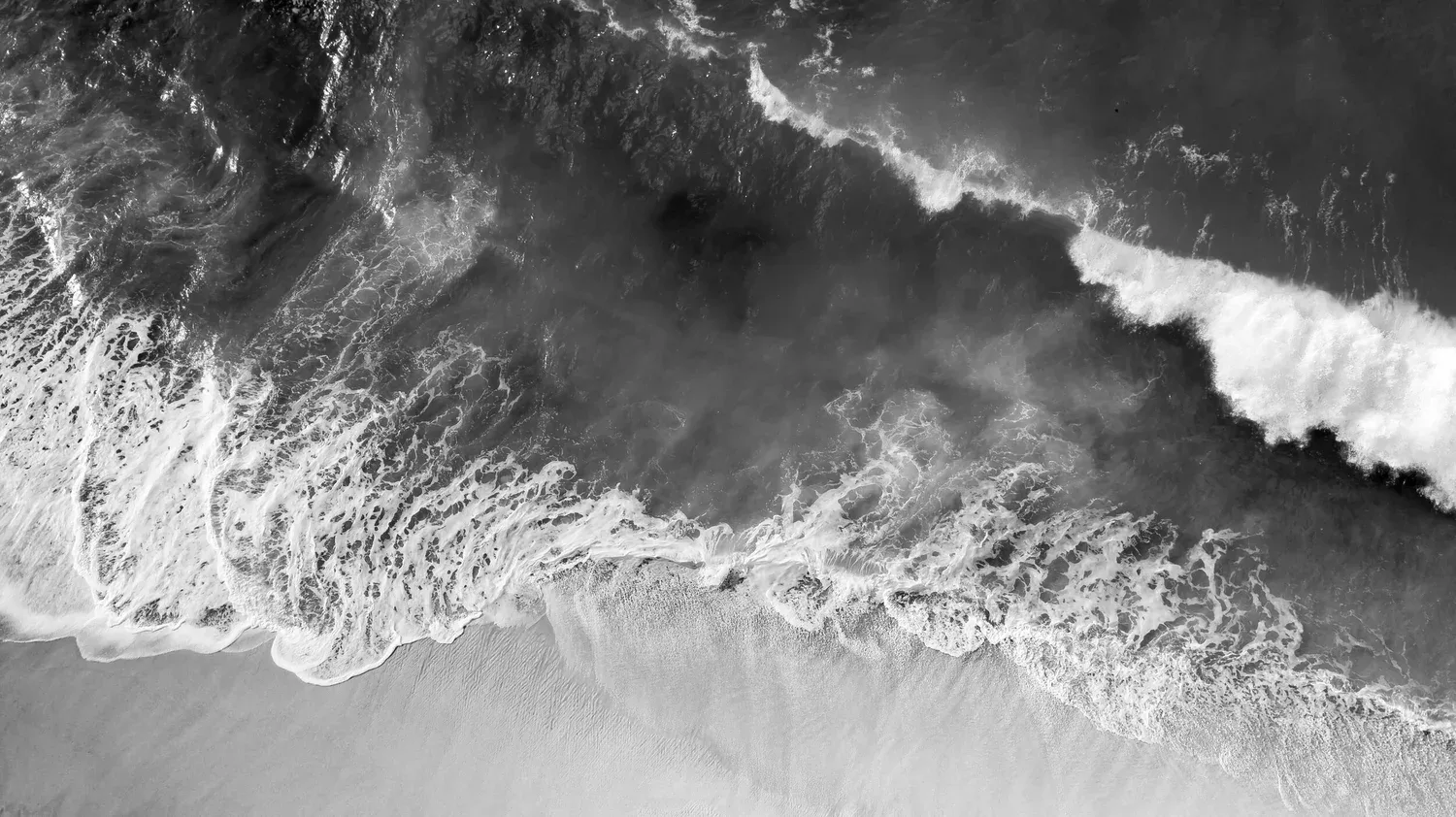 Black-and-white aerial photo of waves meeting the shore