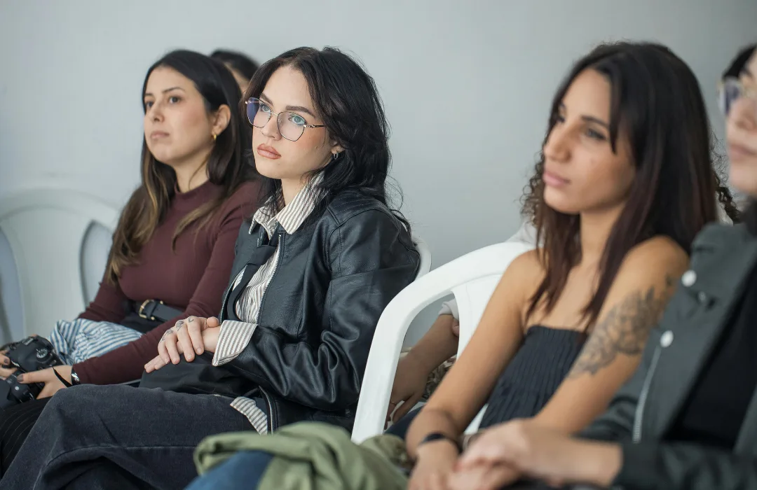 Three young women sitting in chairs listening attentively in a group setting