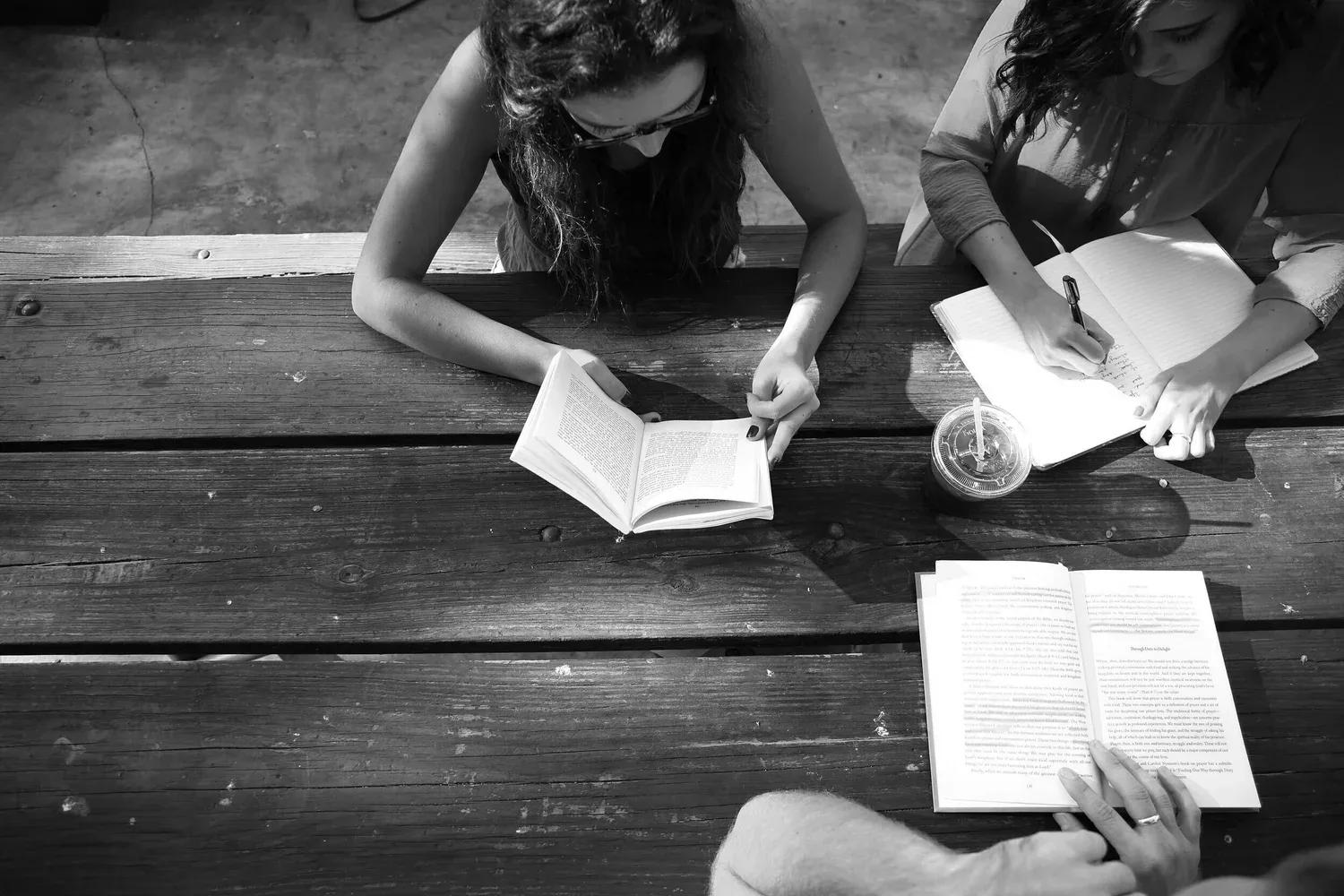 Black-and-white overhead photo of two people reading at a wooden table