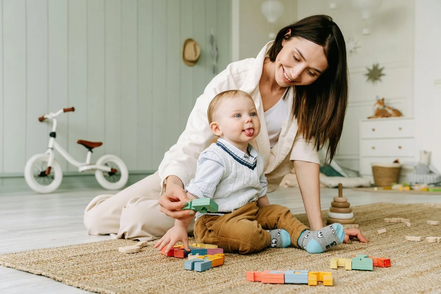 Mother playing with her baby on a rug surrounded by toys