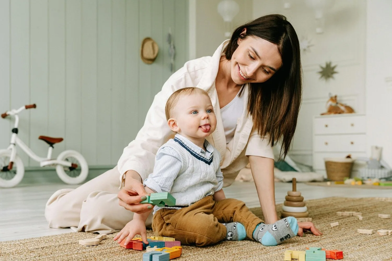 Mother playing with her baby on a rug surrounded by toys