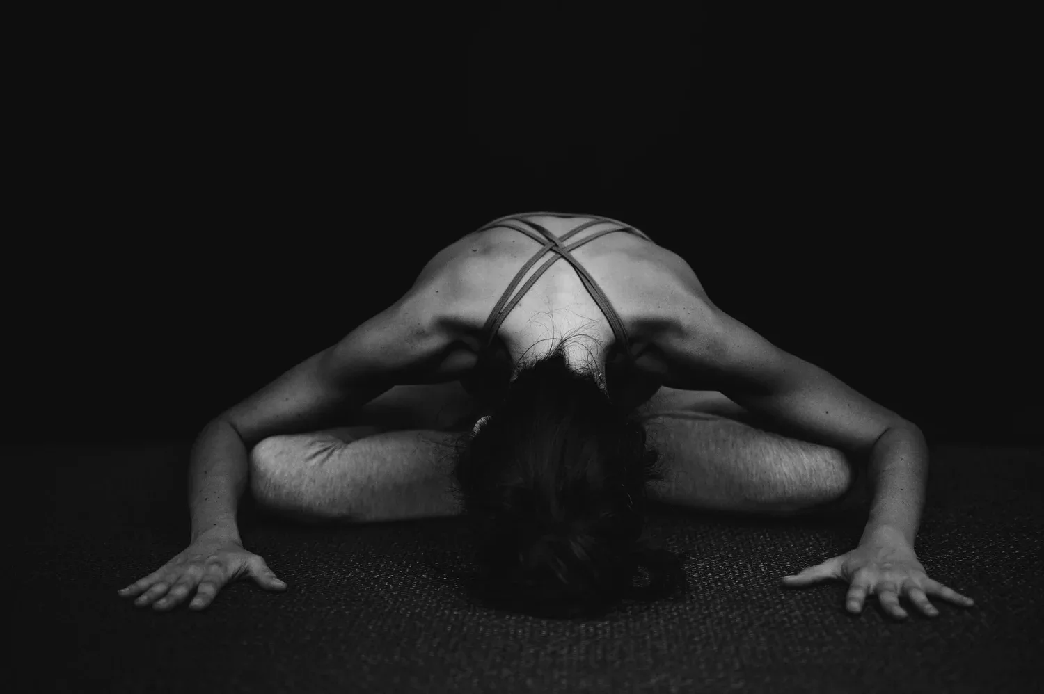 Black-and-white photo of a person in a deep forward stretch on the floor