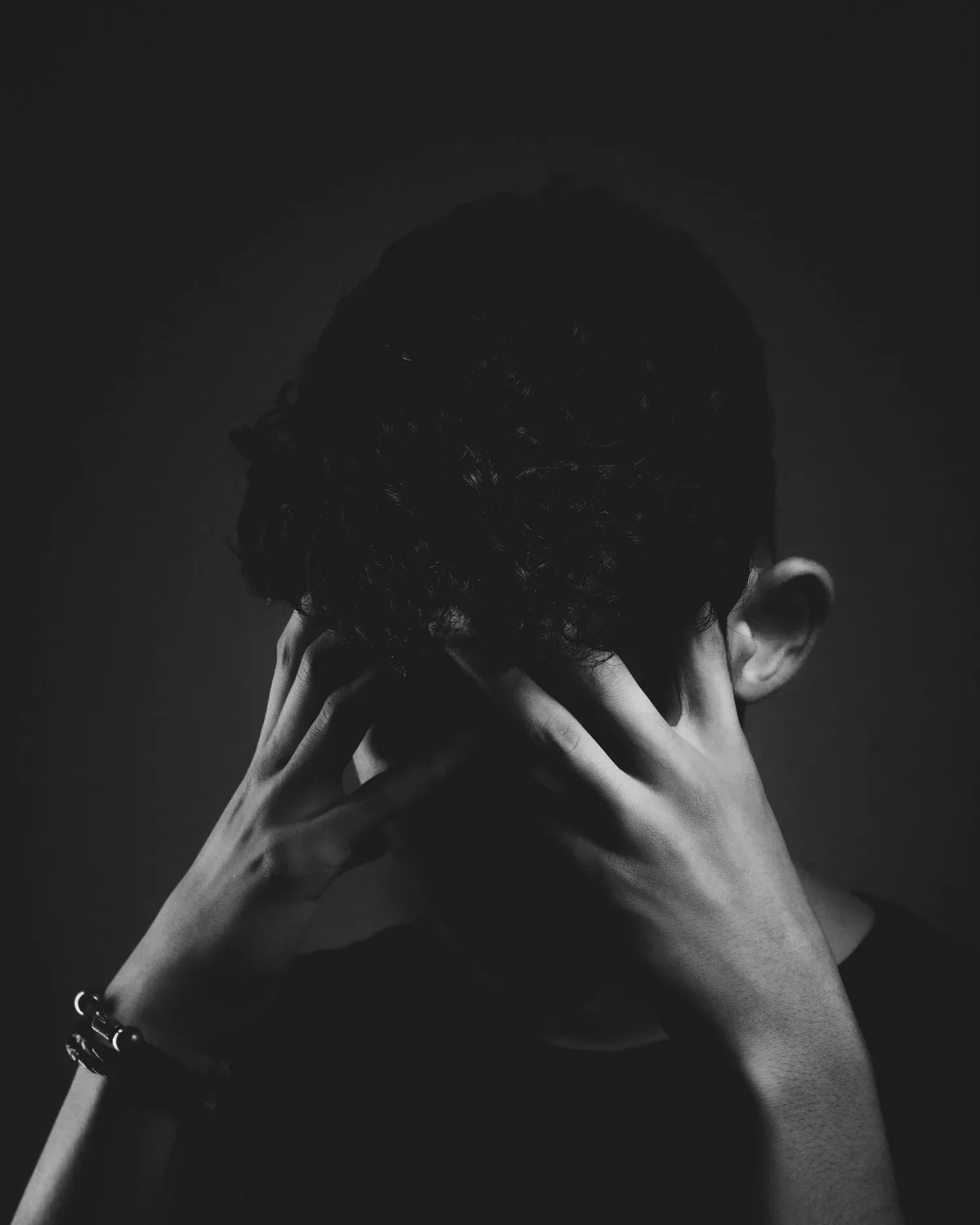 Black-and-white photo of a person holding their head with both hands in shadow