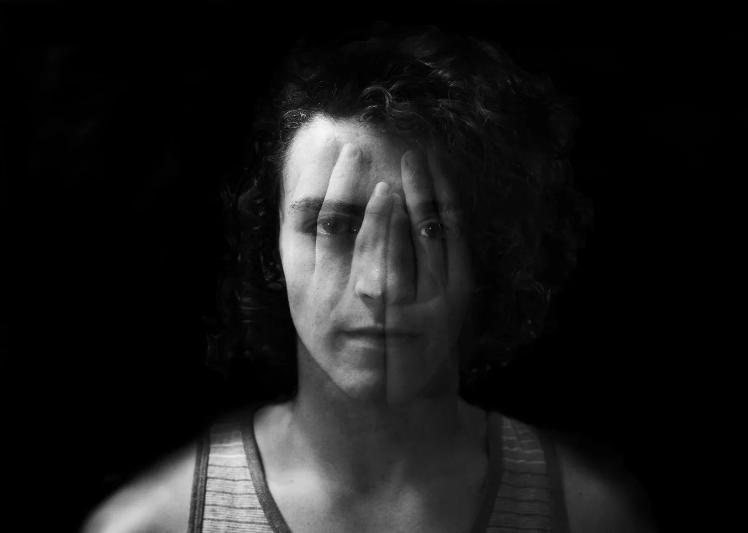 Black-and-white portrait of a woman with curly hair emerging from shadow