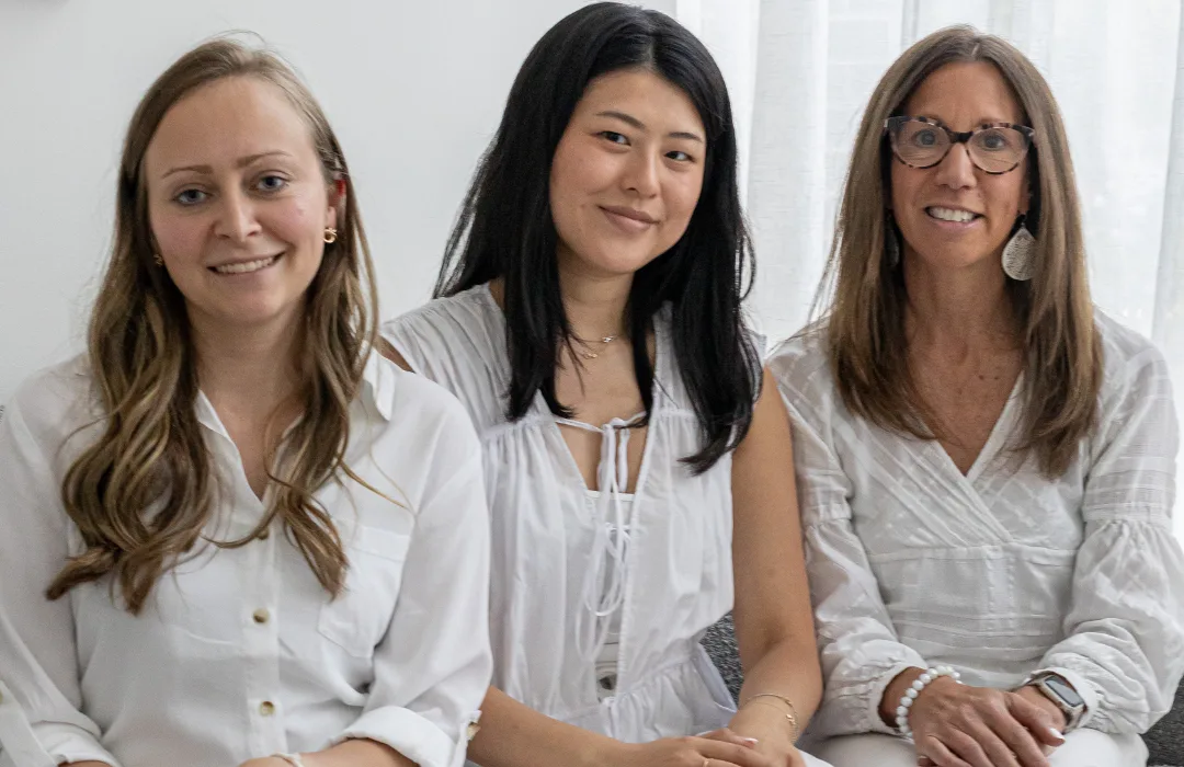 Three smiling women in white seated together on a sofa