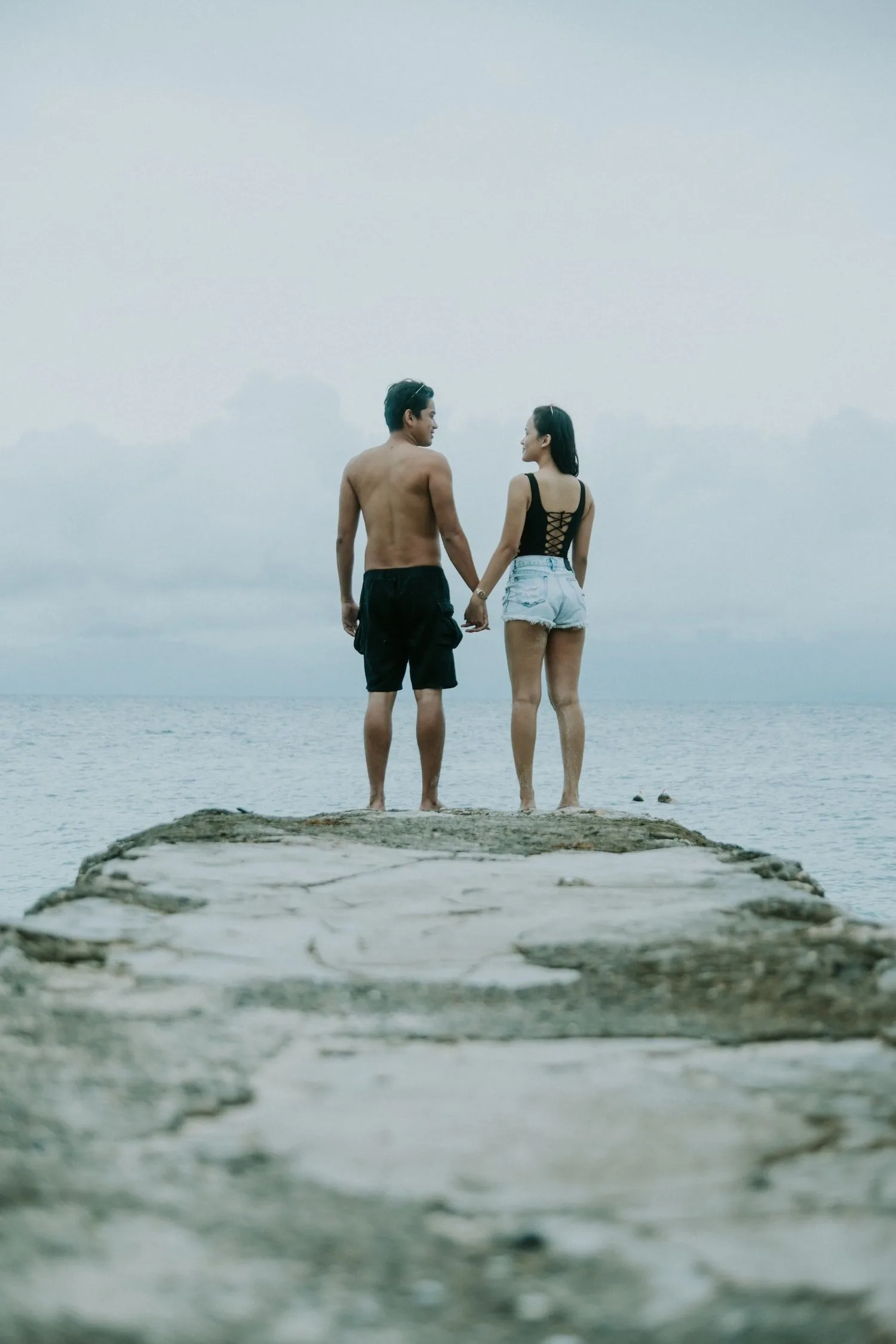 Two people standing together on a rocky point looking out at a misty sea