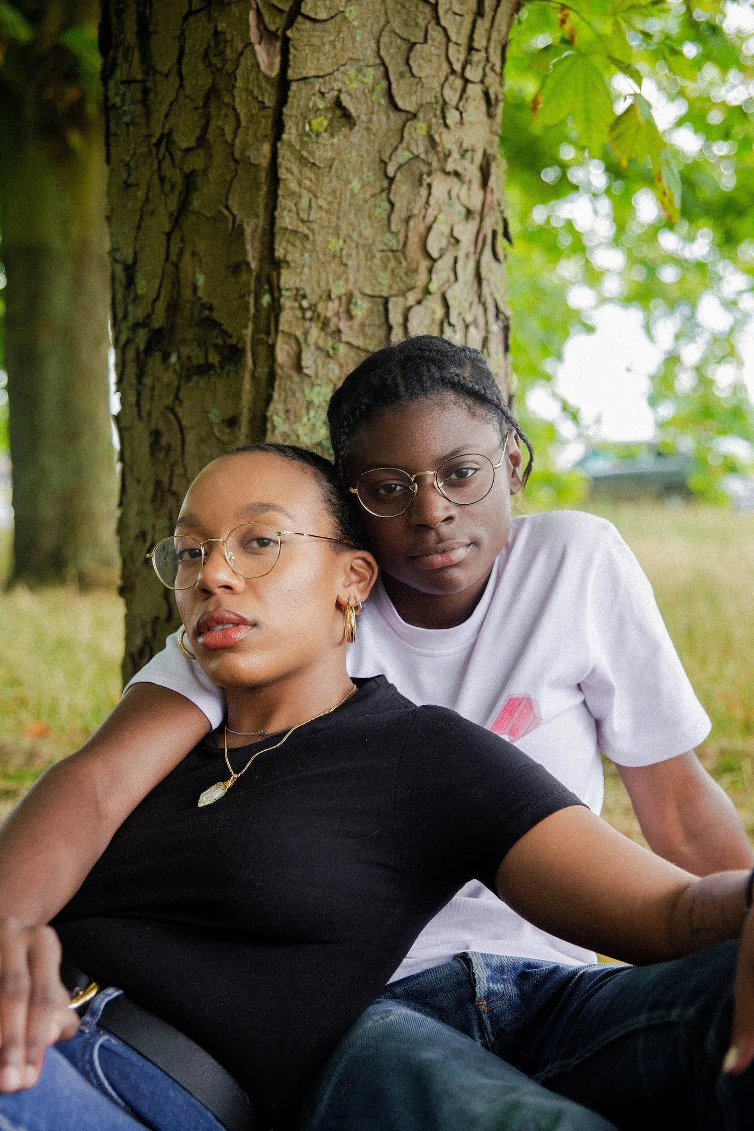Two young women sitting close together under a tree
