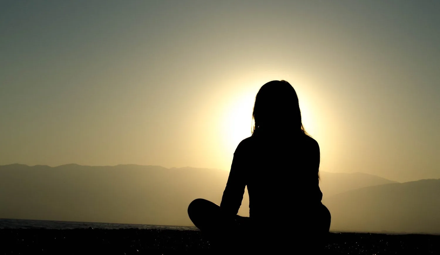 Silhouette of a person meditating against a setting sun