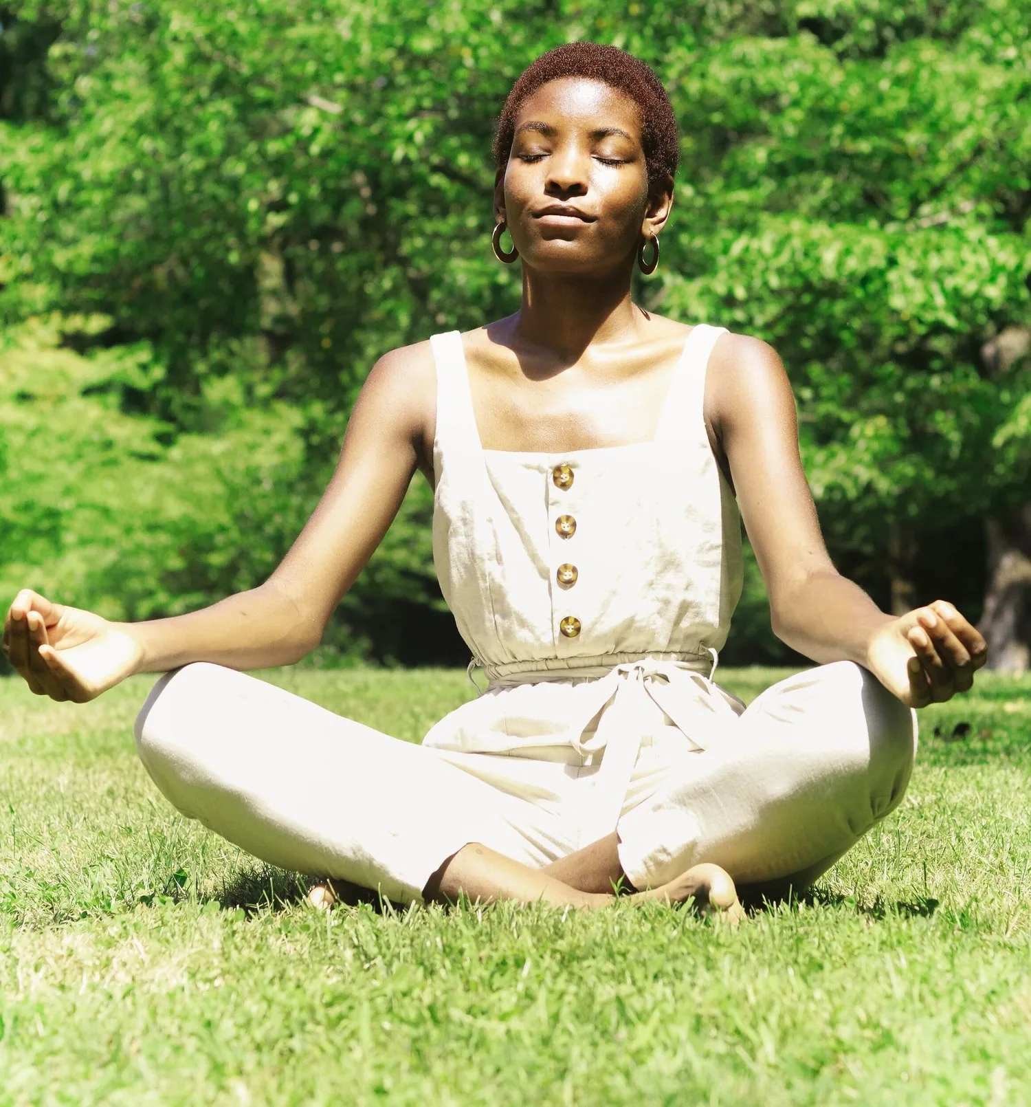 Woman meditating cross-legged on grass in sunlight