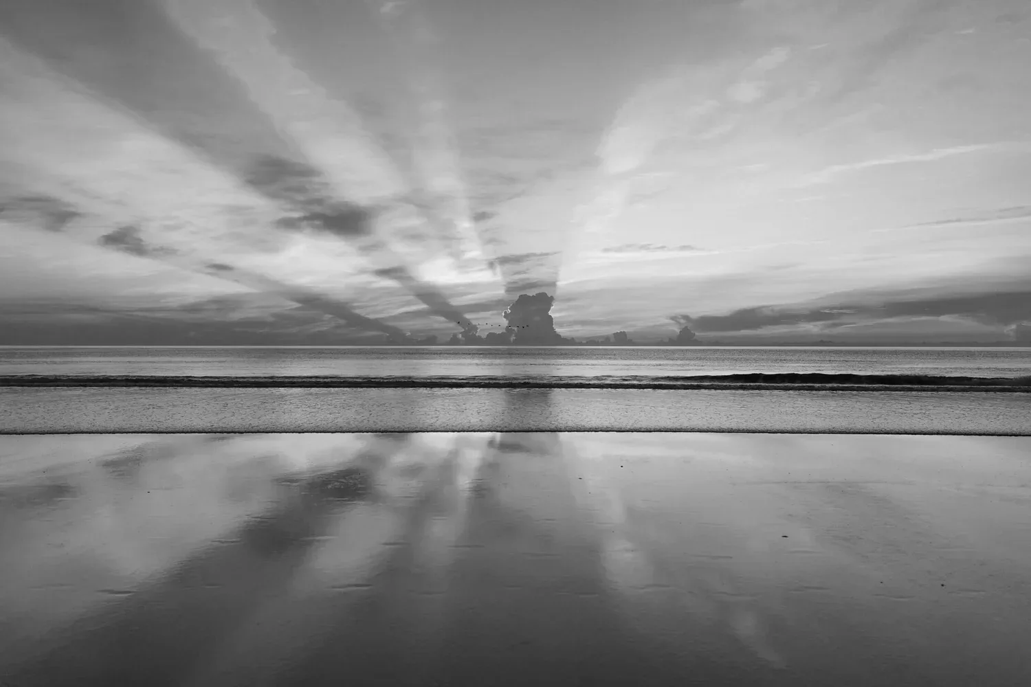 Black-and-white photo of light rays reflected over calm water