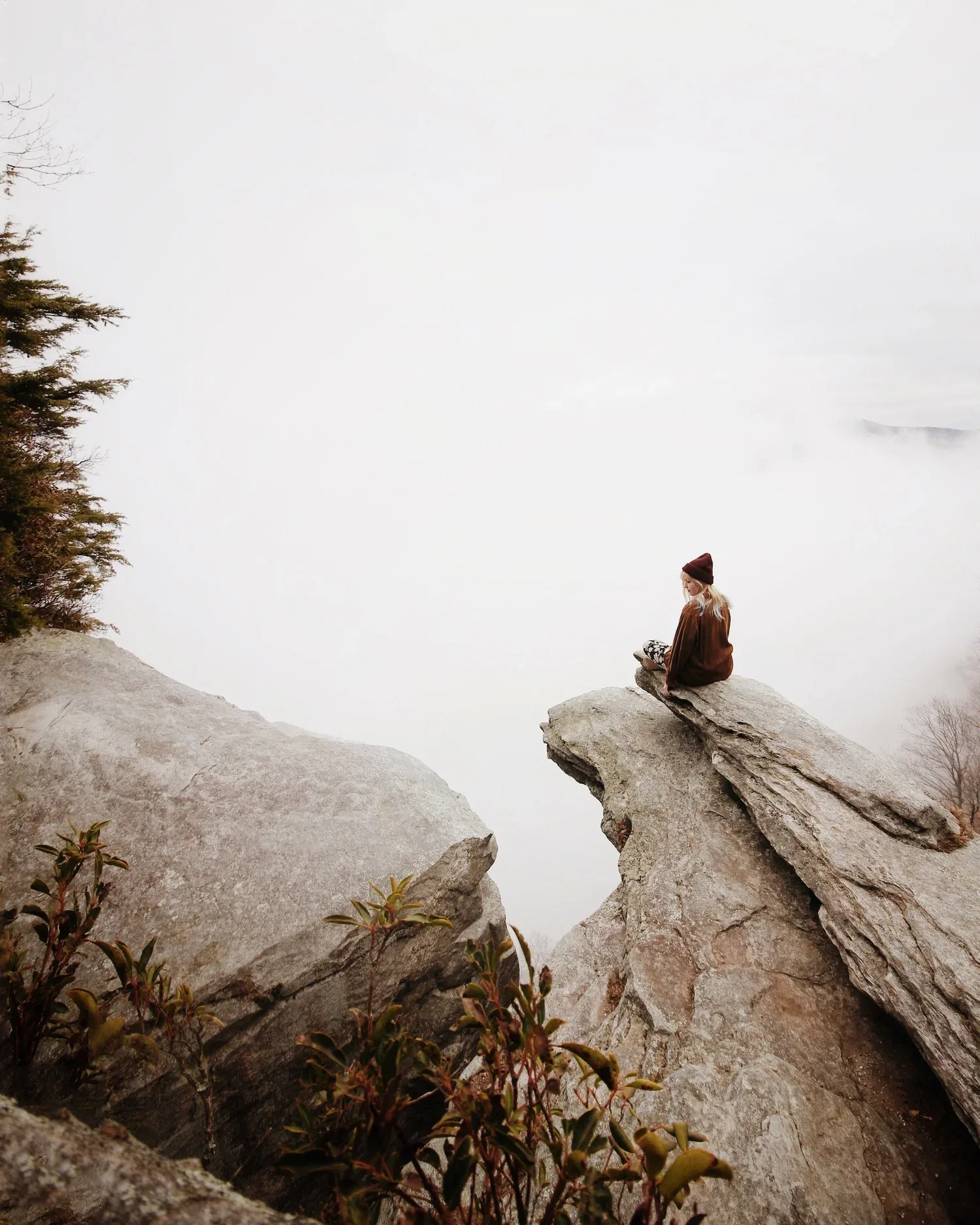 Person sitting alone on a high rock above a foggy valley