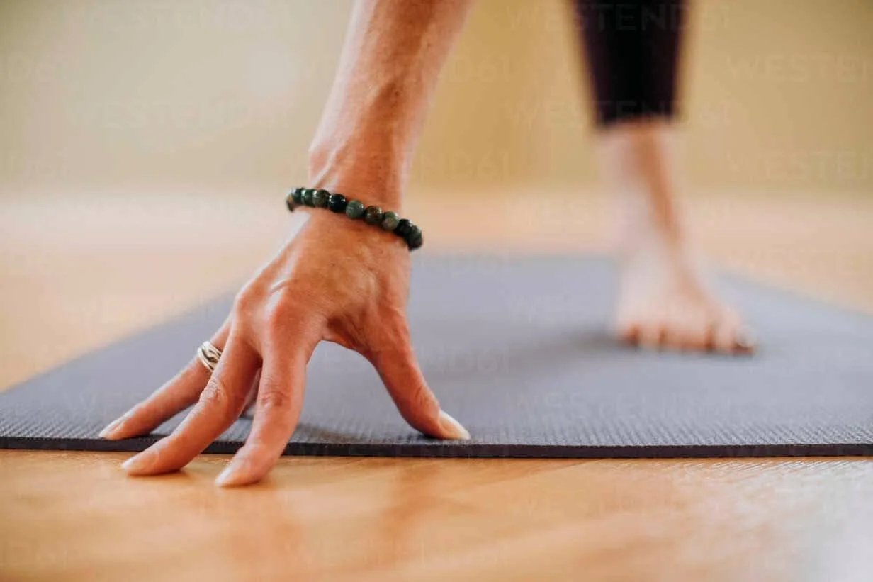 Hands resting on a yoga mat with bare feet in the background
