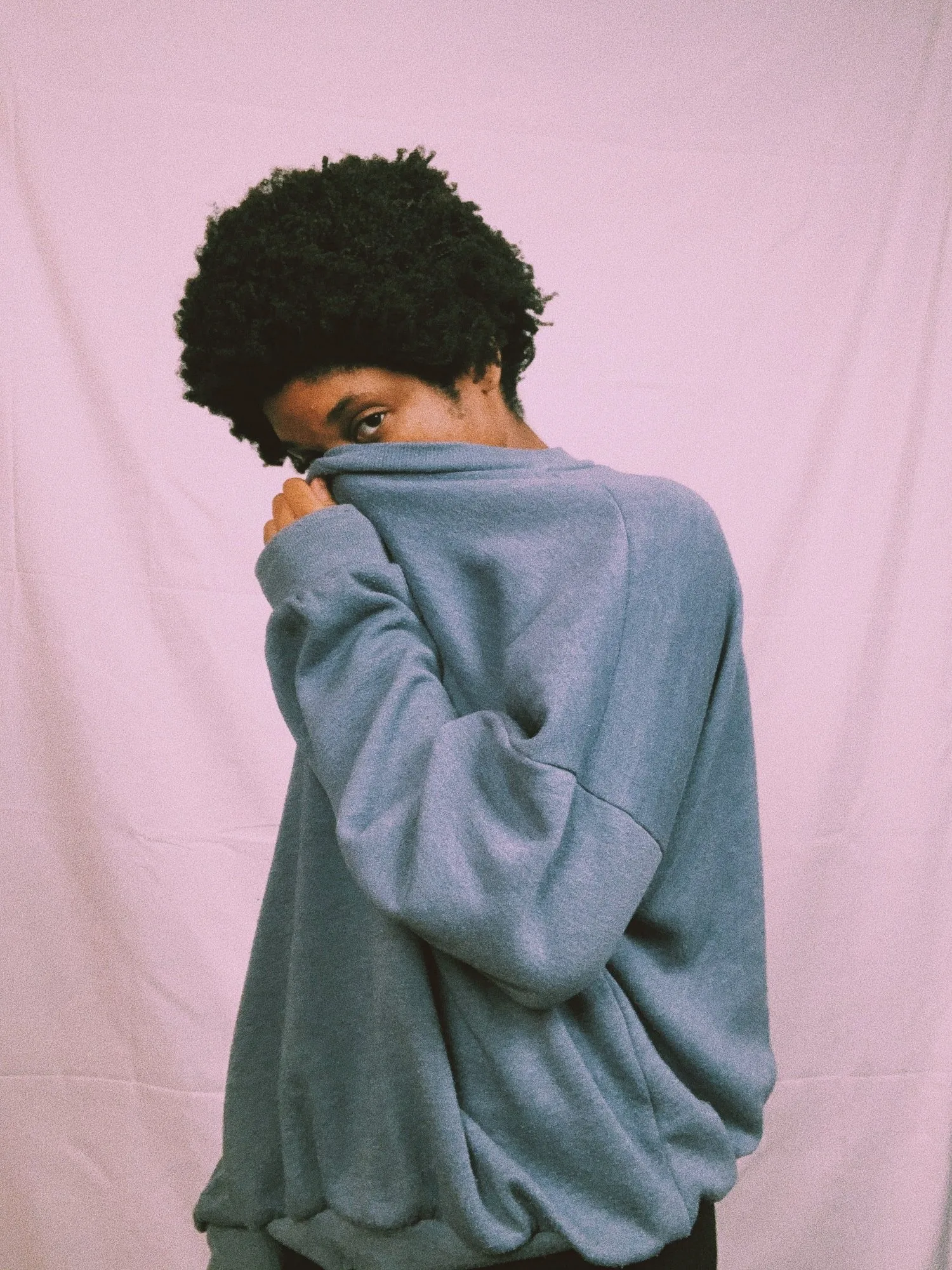 Person in a gray sweater pulling the collar up over their face