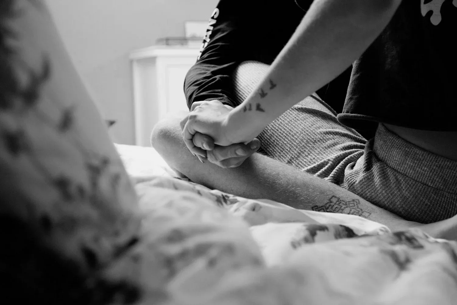 Black-and-white photo of hands resting on a rumpled bed