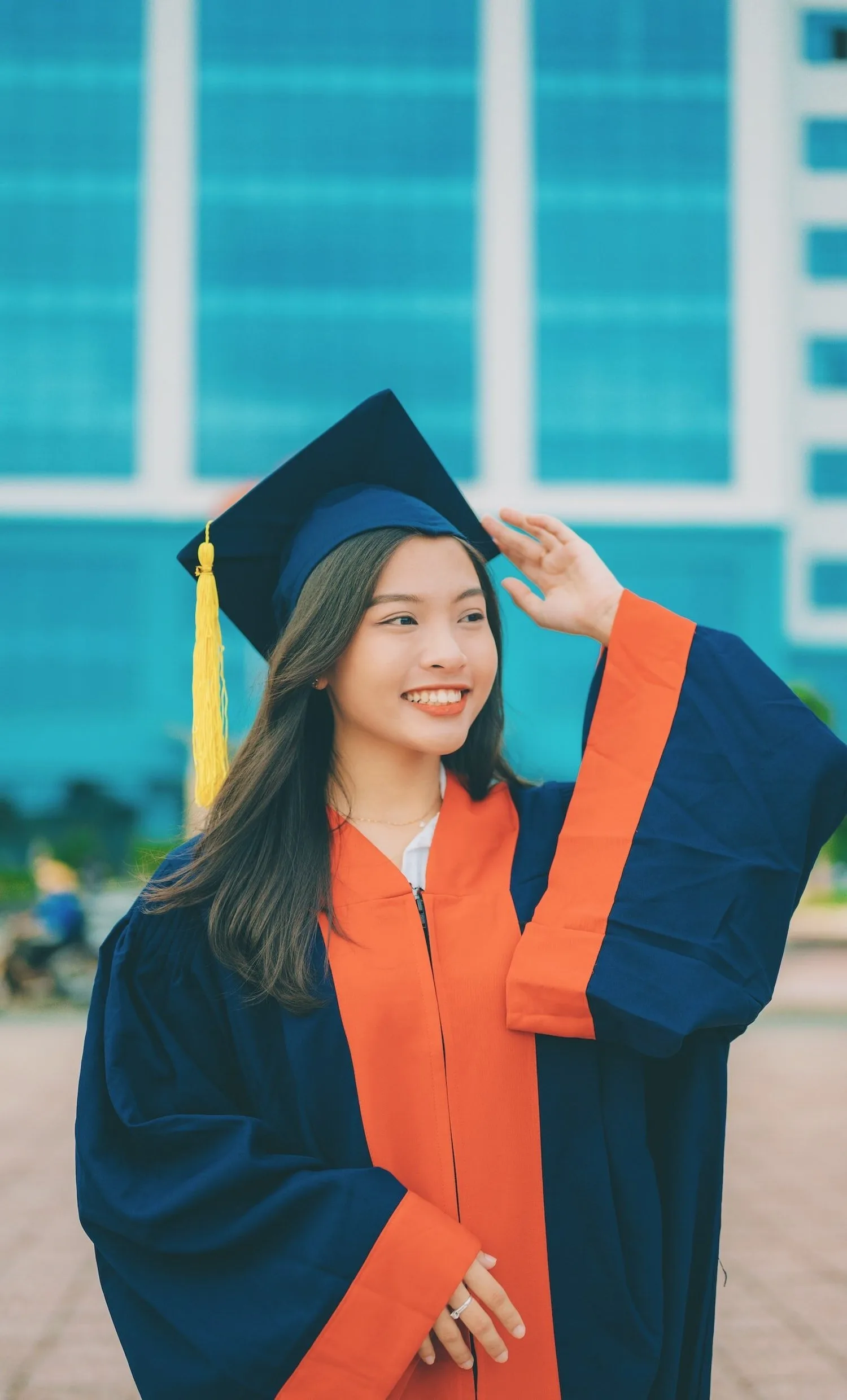 Smiling graduate in a cap and gown standing in front of a glass building