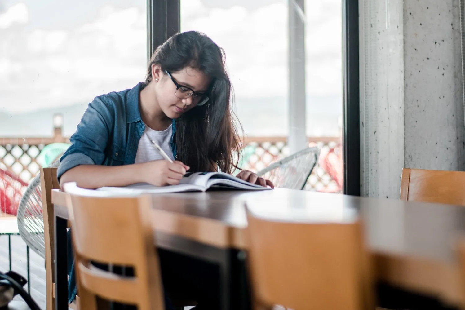 Woman in glasses writing in a notebook at a café table