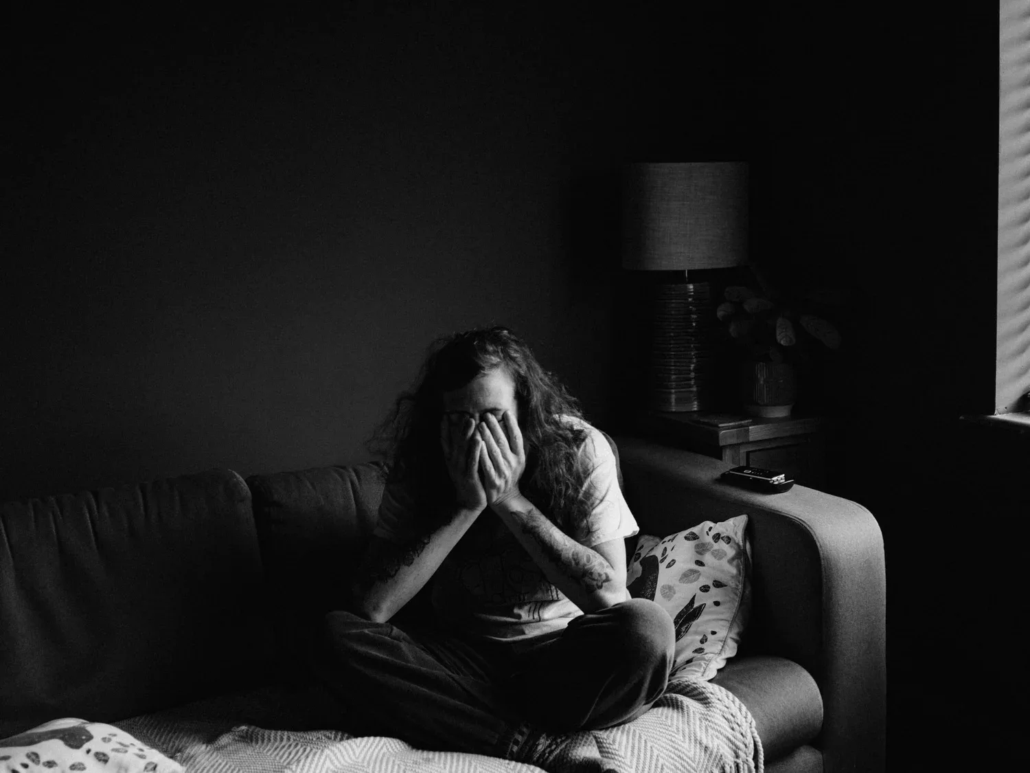 Black-and-white photo of a person sitting on a sofa with head in hands