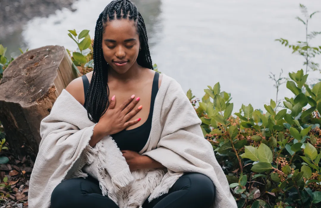 Woman wrapped in a blanket outdoors with one hand resting on her chest, eyes closed