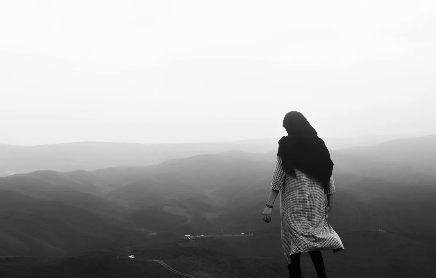 Black-and-white photo of a woman standing alone on a hillside facing the horizon