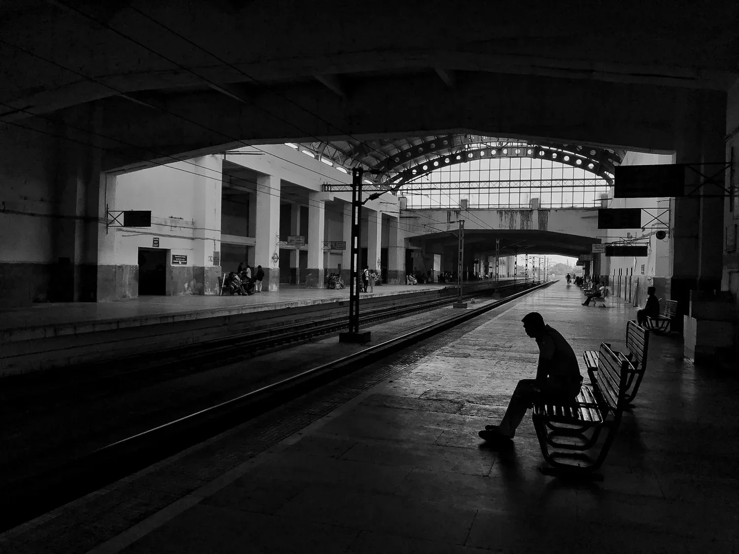 Black-and-white photo of a person sitting alone on a bench in an empty train station