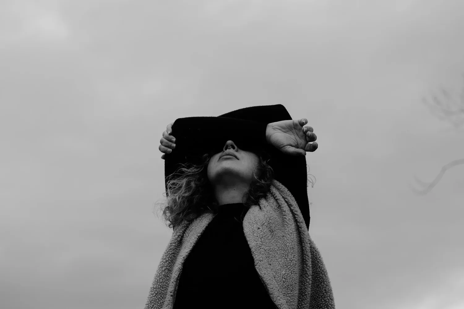 Black-and-white photo of a person with arms raised over their face against a pale sky