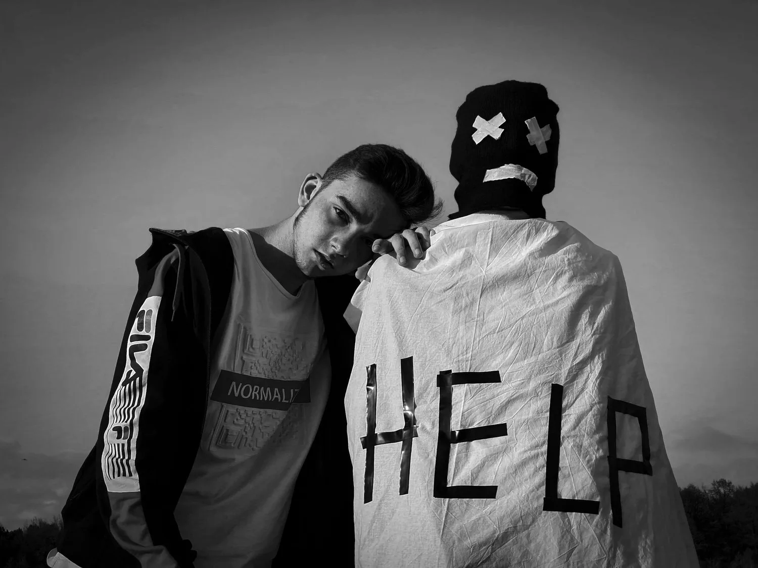 Black-and-white photo of two people, one wearing a jacket with HELP written on the back