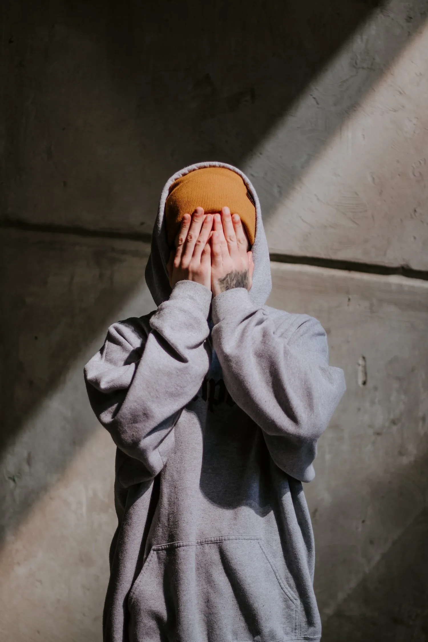 Person in a hoodie covering their face with both hands