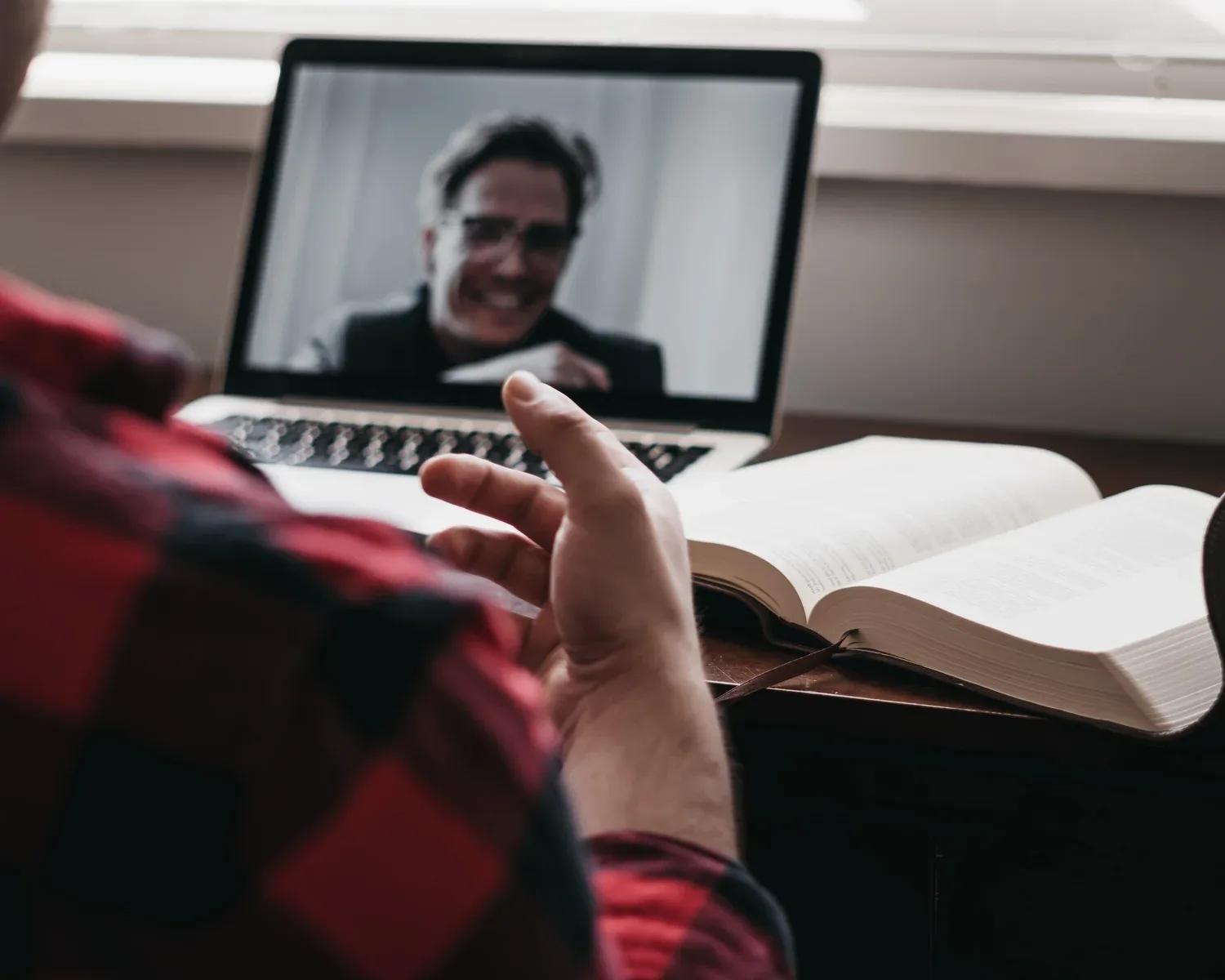 Person on a video call with a smiling therapist on a laptop screen