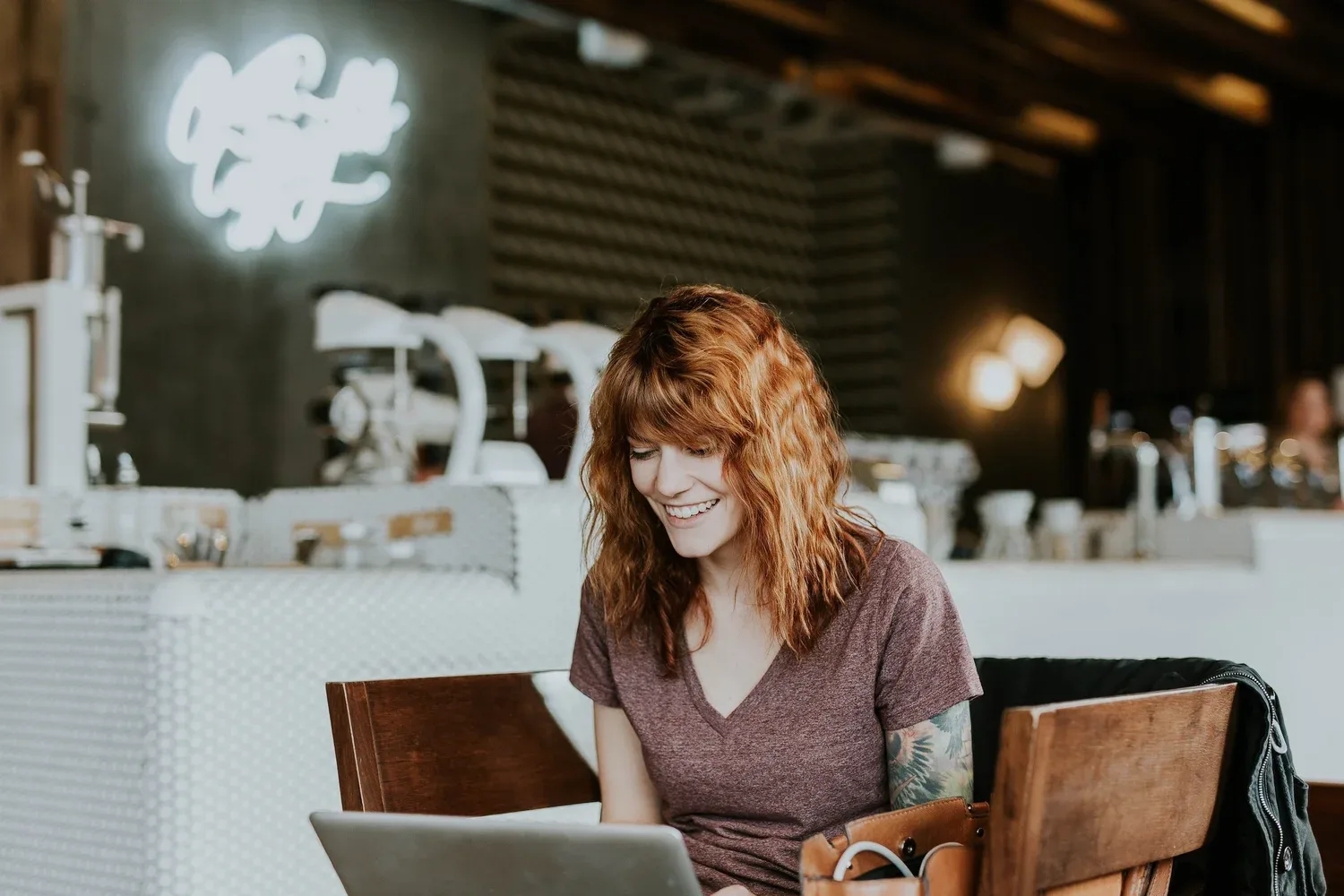 Woman with red hair working at a laptop in a warmly lit café