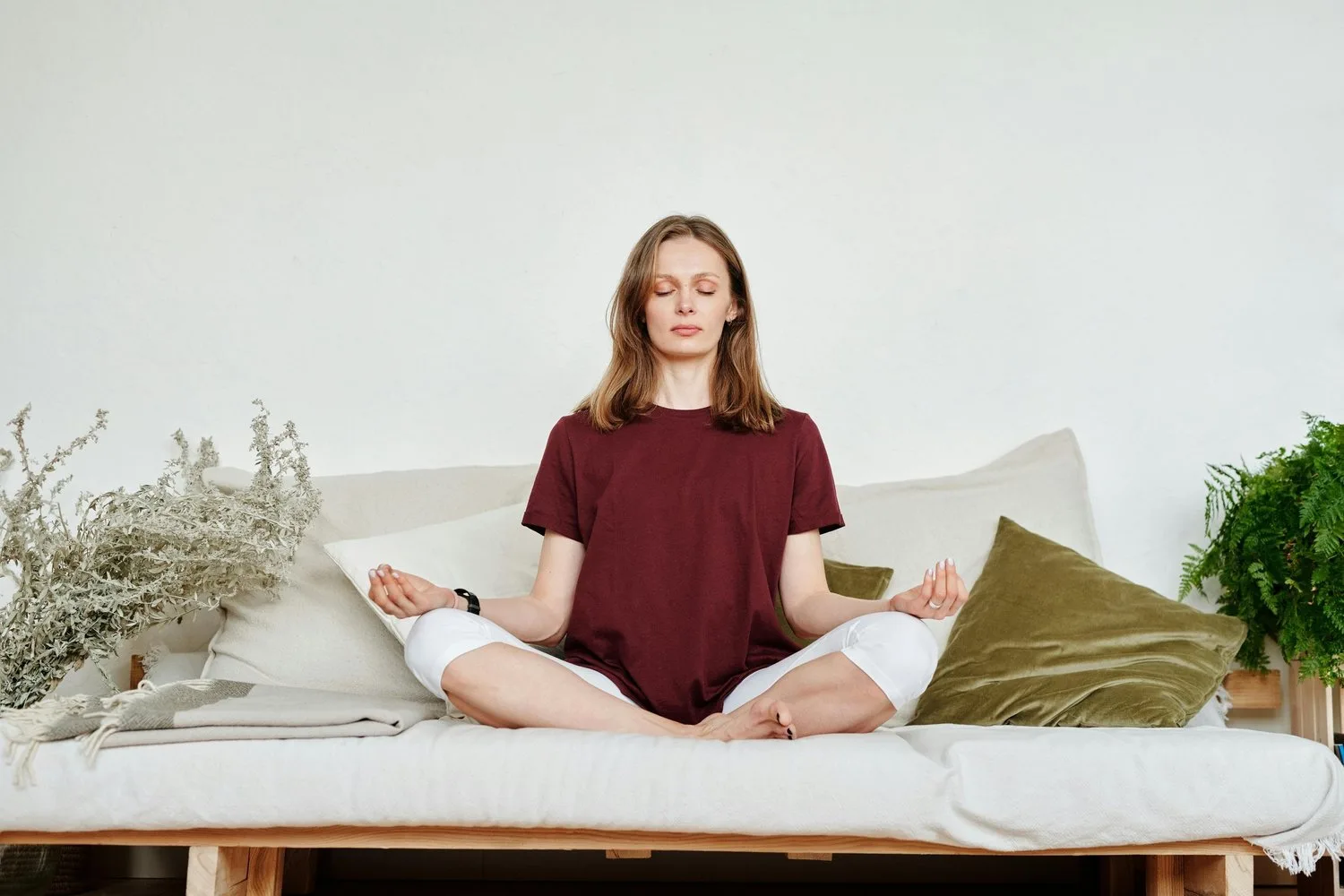 Woman in a red top meditating cross-legged on a bed with eyes closed