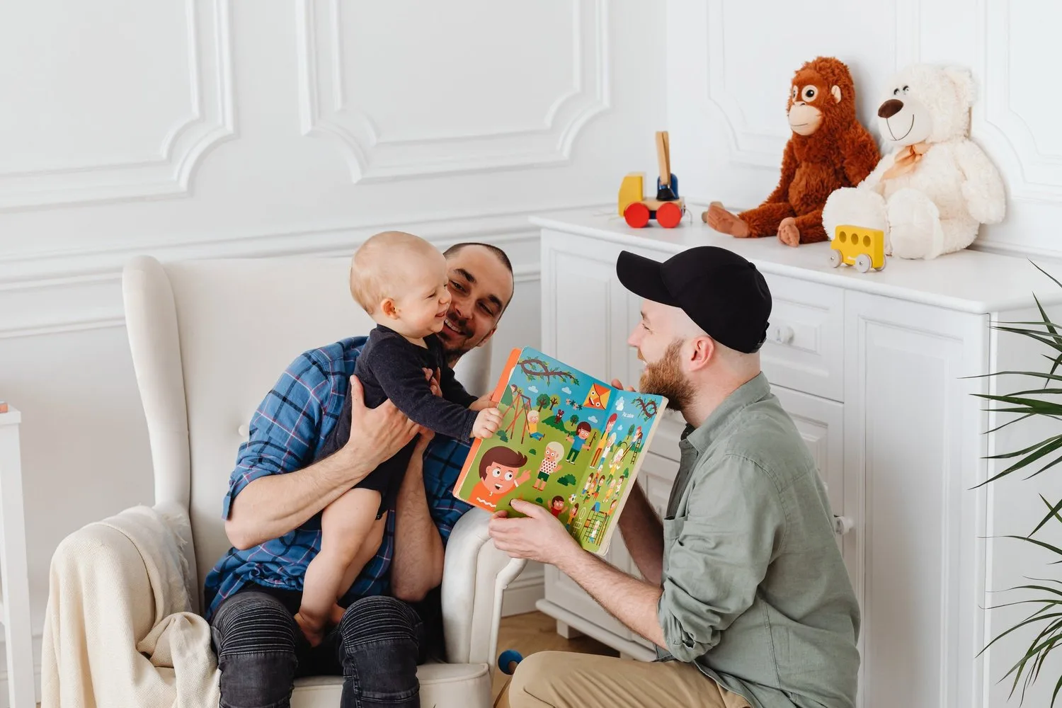 Two fathers reading a picture book with their young child on a sofa