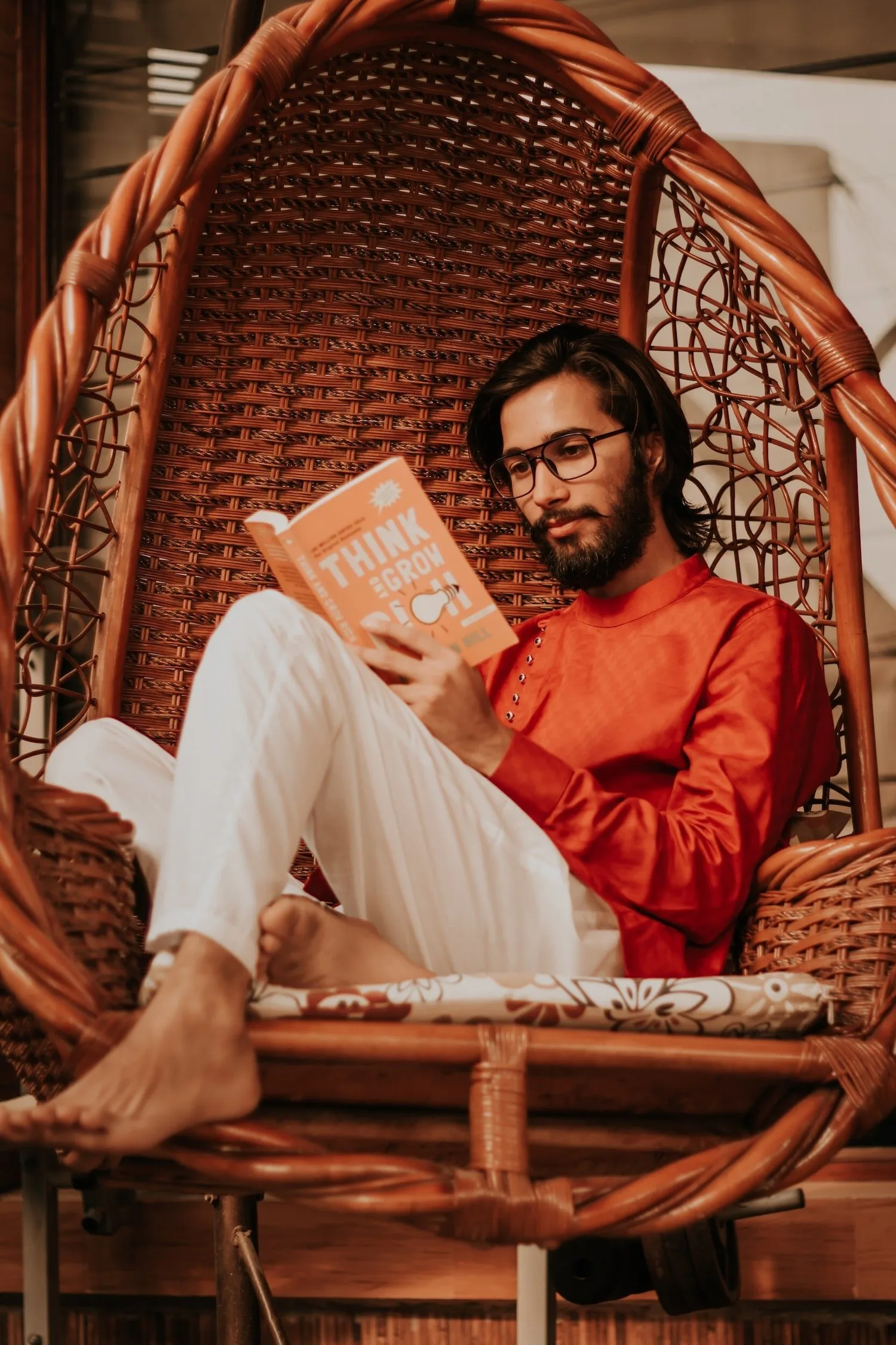 Man in glasses reading in a rattan hanging chair
