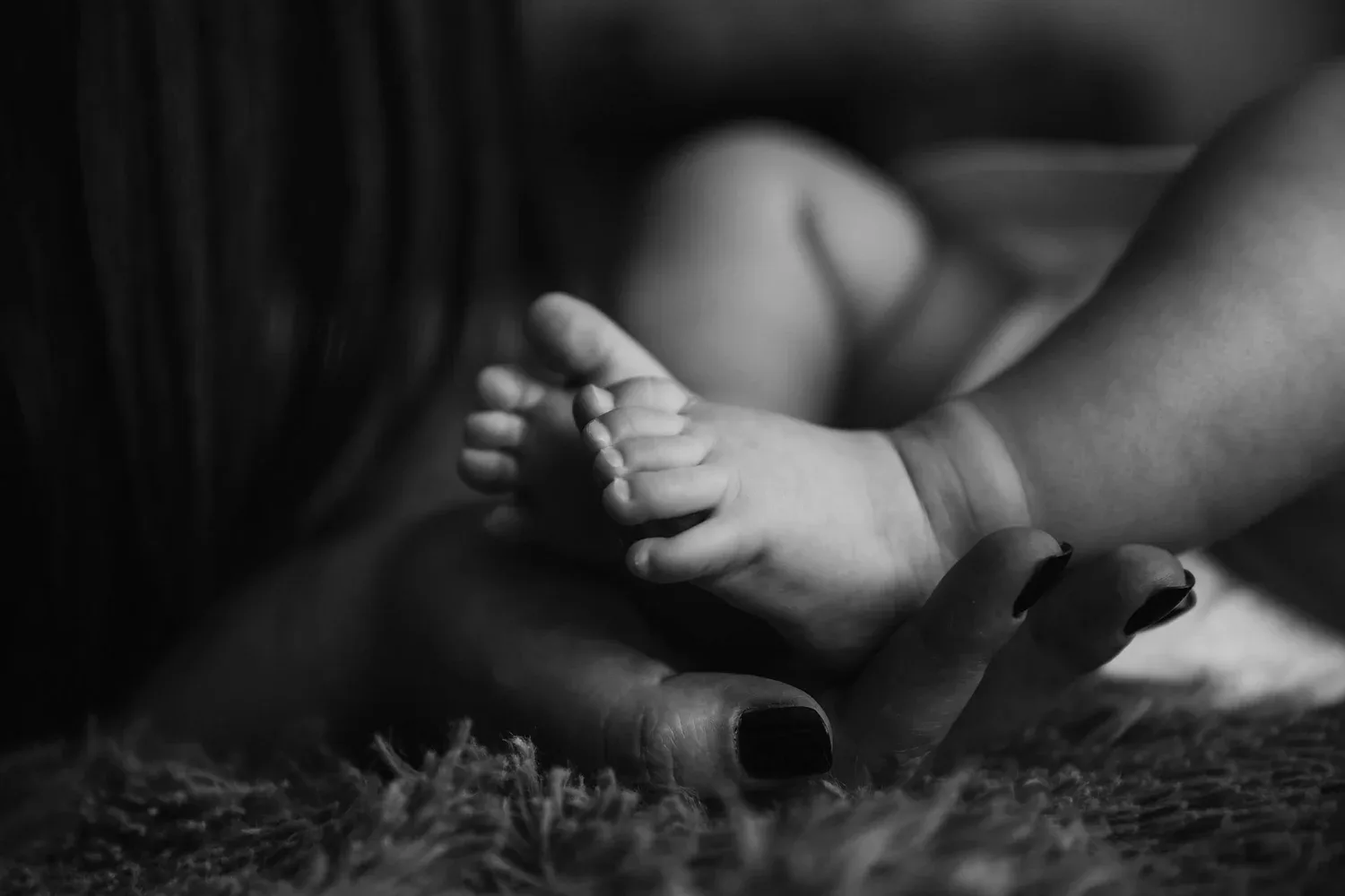 Black-and-white close-up of a baby’s feet held in an adult’s hands