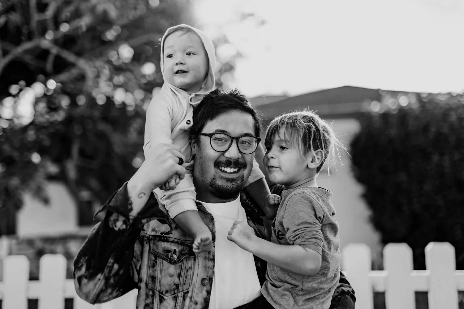 Black-and-white photo of a smiling father carrying his children