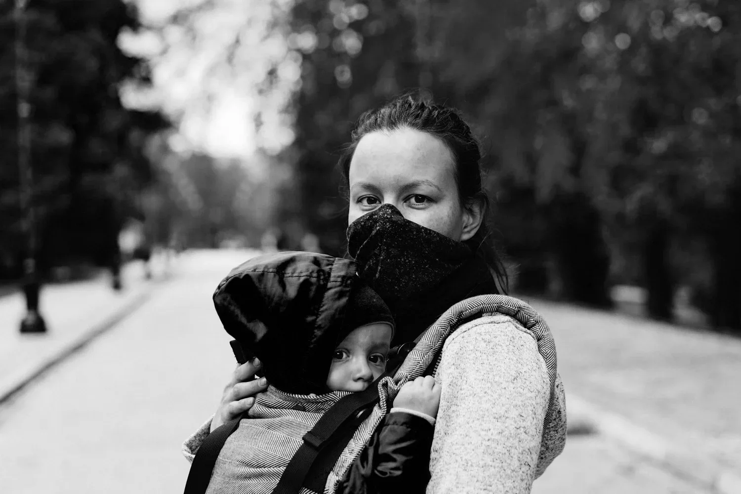 Black-and-white photo of a mother in a face mask carrying her baby outdoors