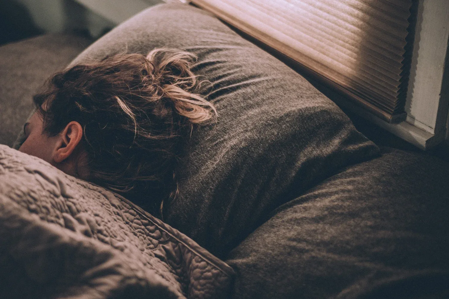 Person lying in bed with their face buried in a pillow