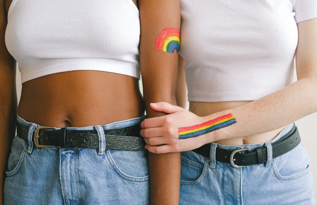 Two people in white tops and jeans, one with a small rainbow painted on their arm