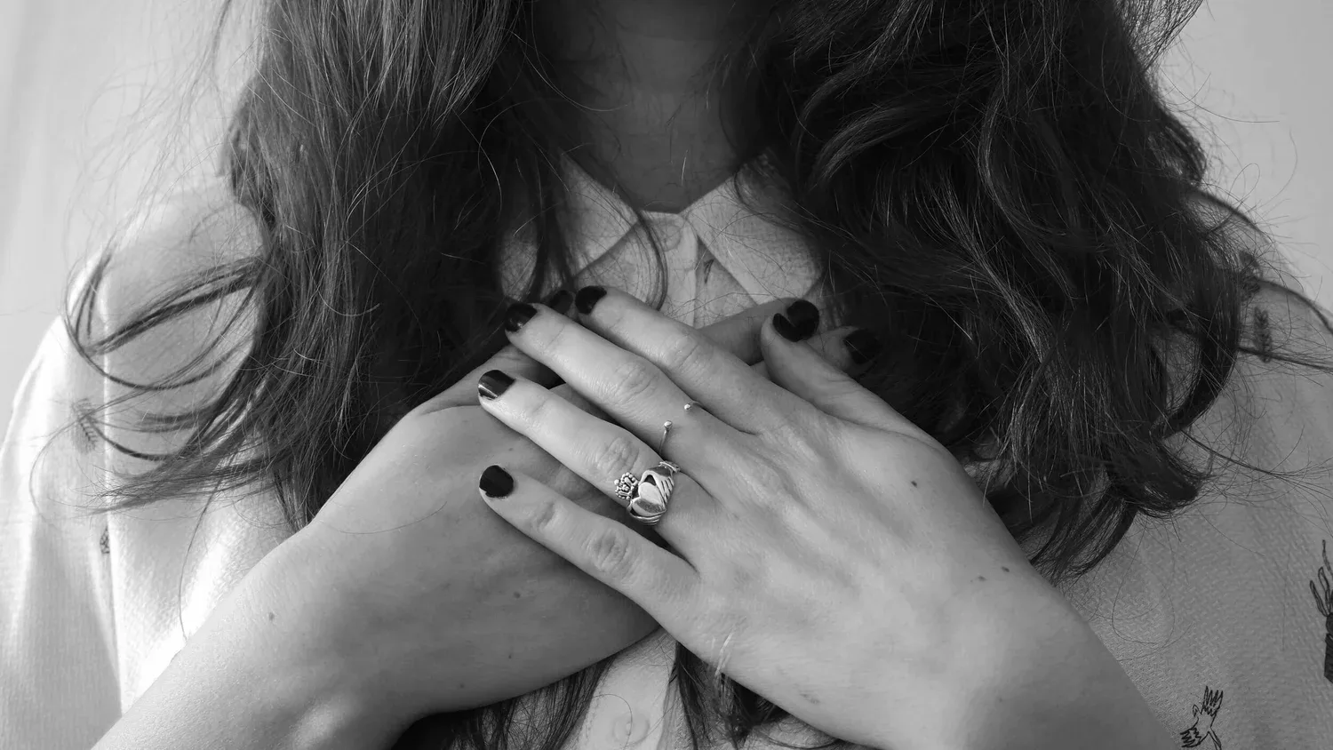 Black-and-white close-up of hands with rings resting over the heart