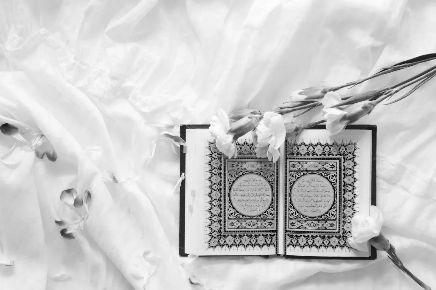 Black-and-white photo of an ornate Quran resting on white fabric