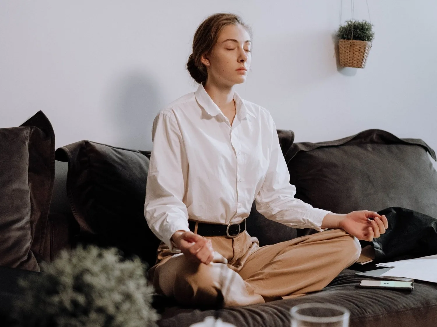Woman meditating cross-legged on a sofa in a calm living room
