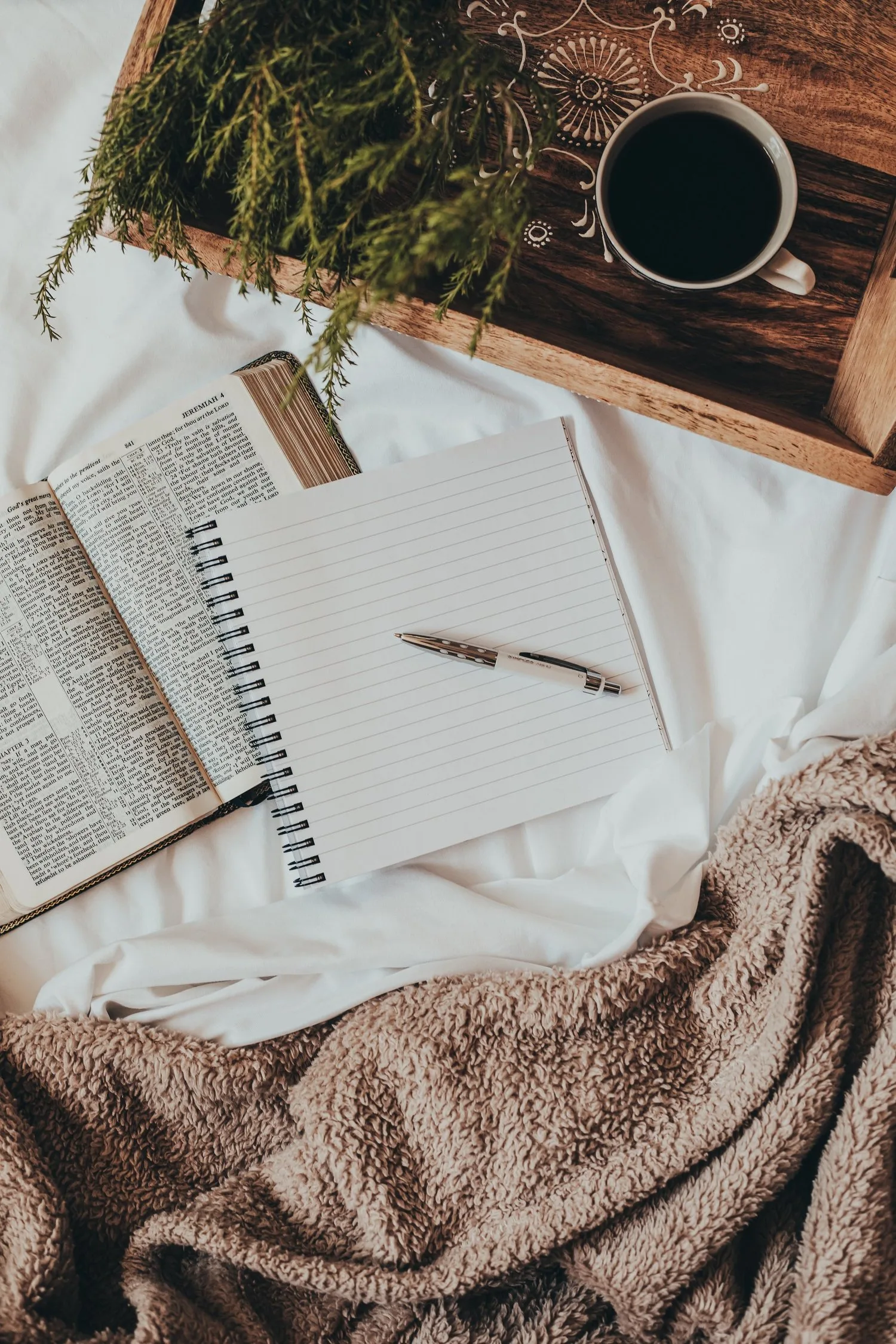 Open book, notebook, and coffee on a cozy knit blanket, seen from above