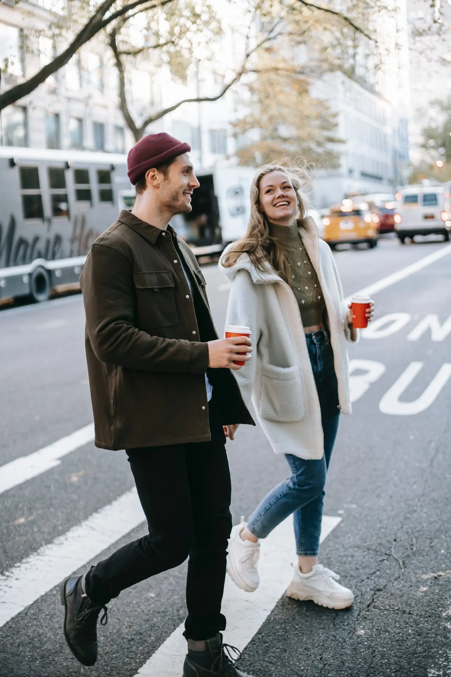 Couple laughing while crossing a busy city street with coffee